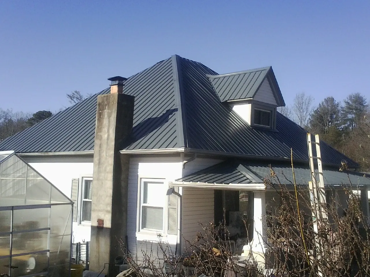 Dark blue standing seam metal roof on a white farmhouse with dormer — Slate & Tile Roof Repair by Roofing Brothers in Monkton