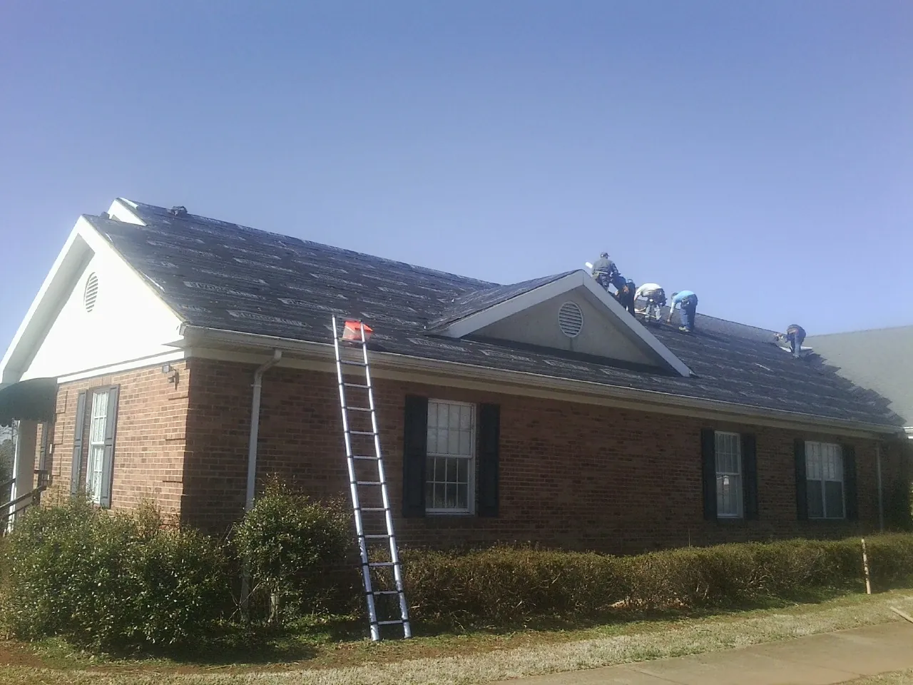 Crew tearing shingles off a brick ranch roof with a ladder set — Emergency Roof Repair work by our crew in Monkton