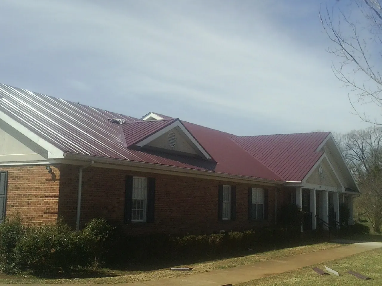 Red metal roof with gabled entries on a long brick building, from a Hail Damage Roof Repair job in Monkton