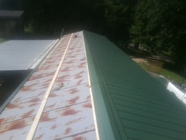 Old rusted panels beside newly installed green metal roofing — Wind Damage Roof Repair by Roofing Brothers in Monkton
