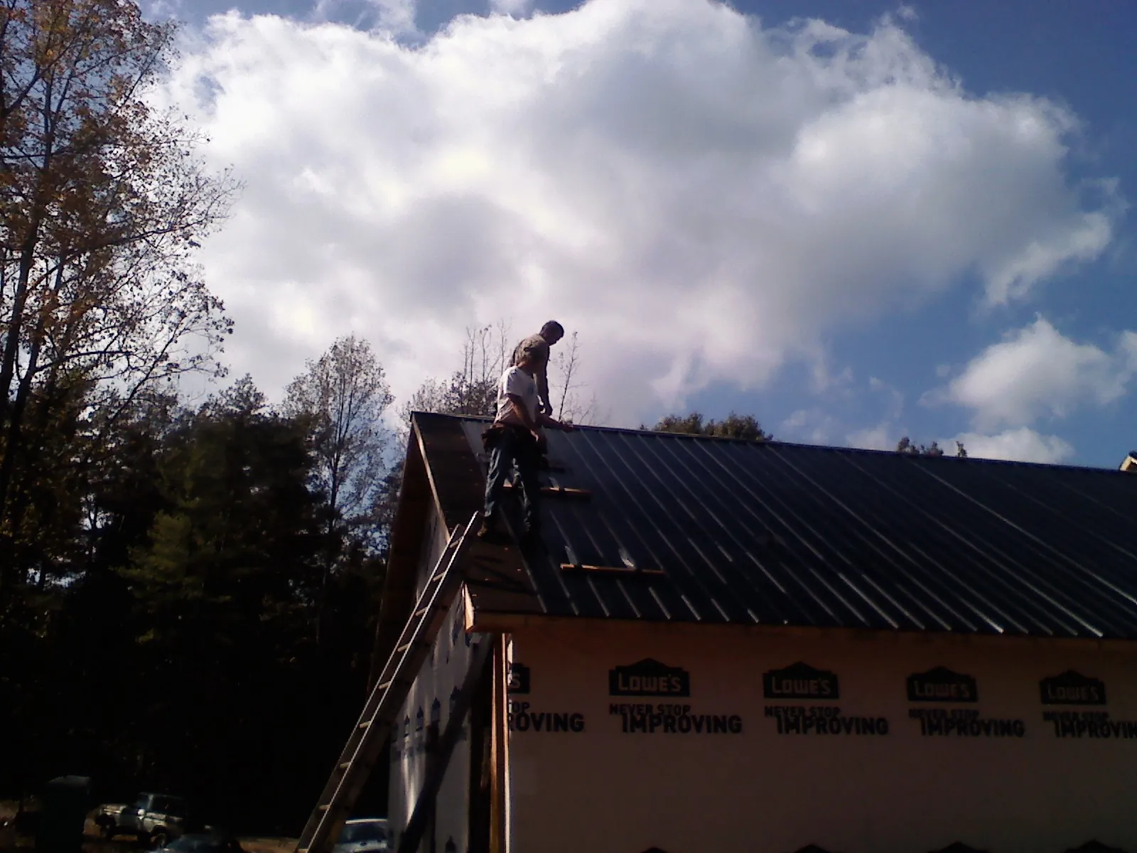 Roofer fastening dark metal panels high against a cloudy sky, from a Roof Inspection job in Monkton
