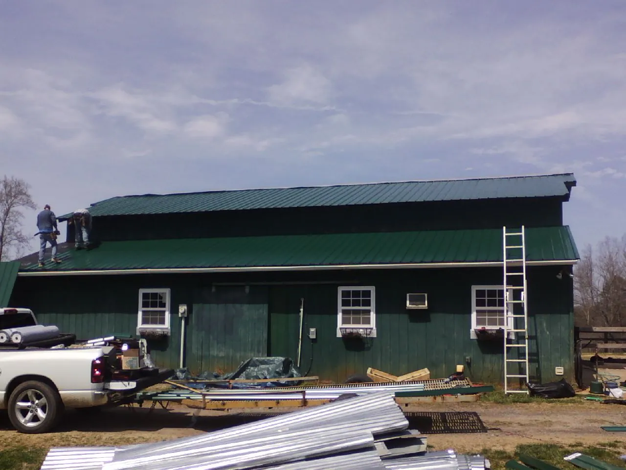 Crew installing green metal roofing on a large green barn in Monkton