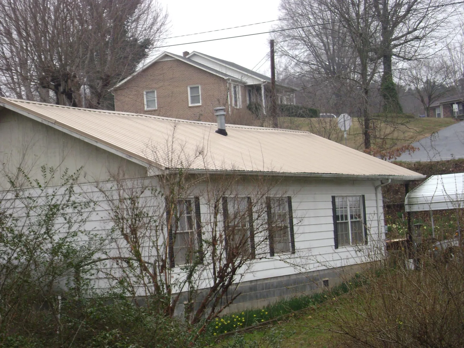 Tan metal roof on a white sided house set into a hillside — Commercial Roofing by Roofing Brothers in Monkton
